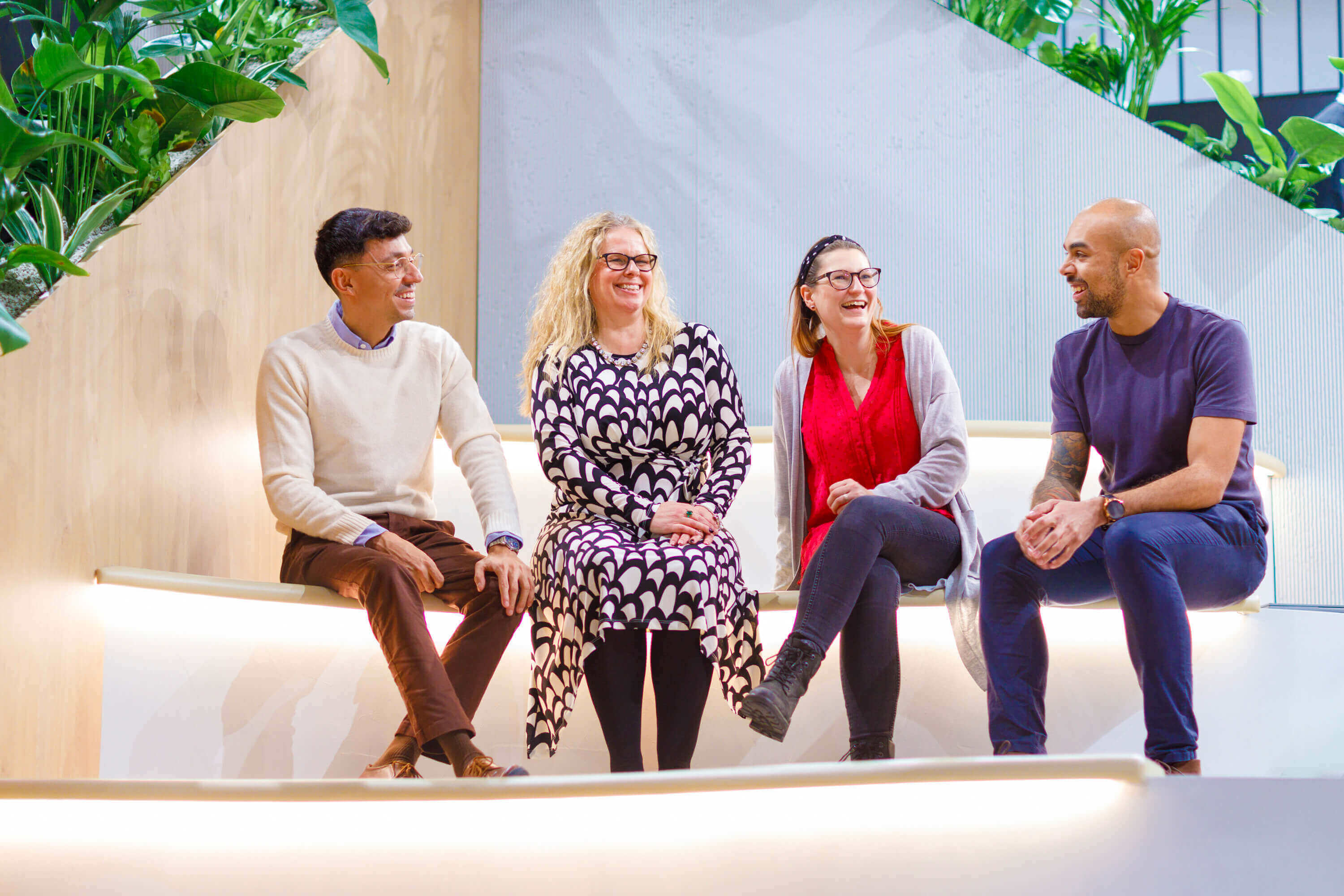 A group of four people, sat together laughing on some steps. There are two men and two women. 