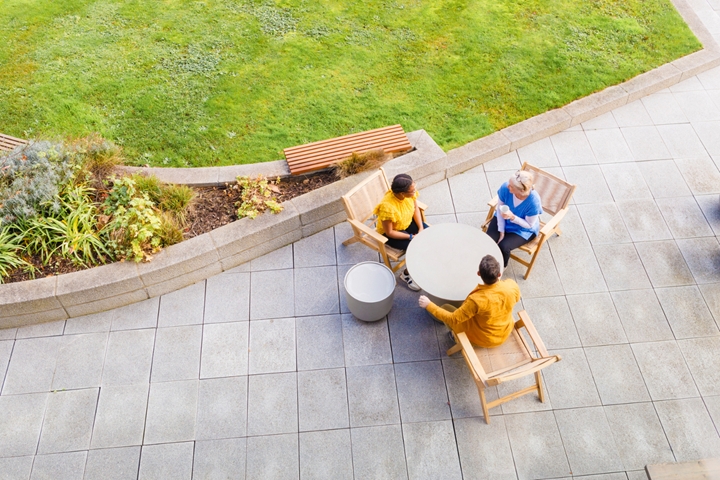 A group of three people, two women and one man, sat outside at a table and having a chat. The photo is shot form above, looking down.