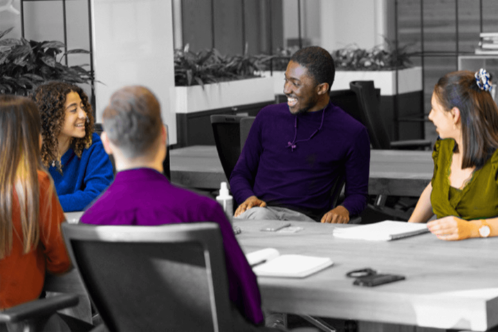 Black and white image, only clothes and skin tone are in colour. A group of five young people work together.
