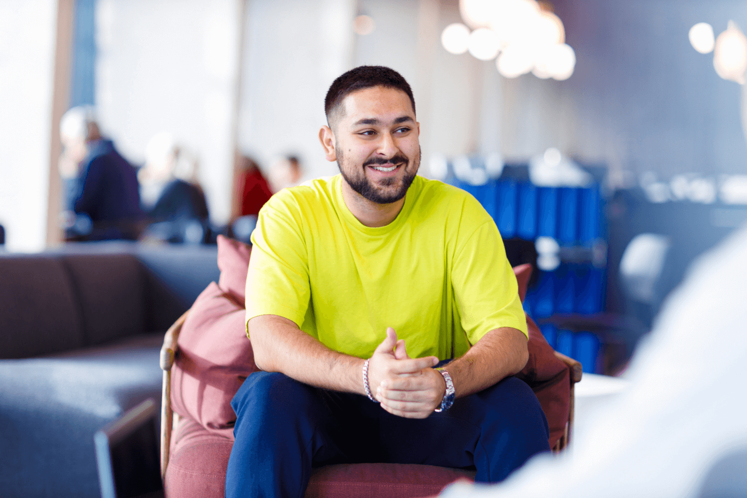 A young man in a yellow T-Shirt, sat on a red chair.