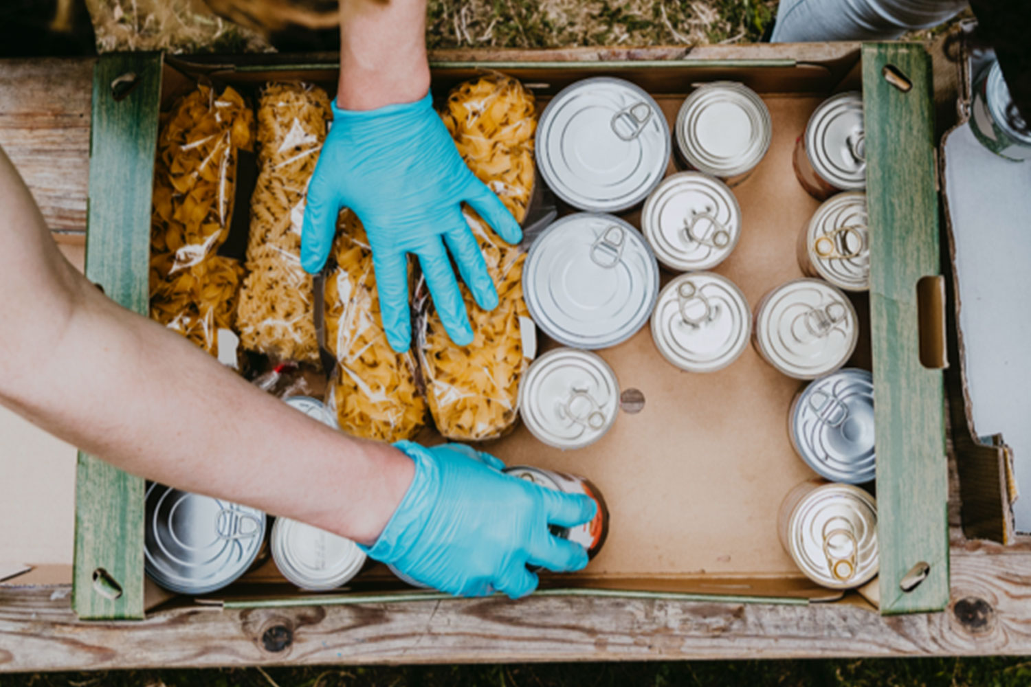 A volunteer with blue gloved hands filling a box with tins.
