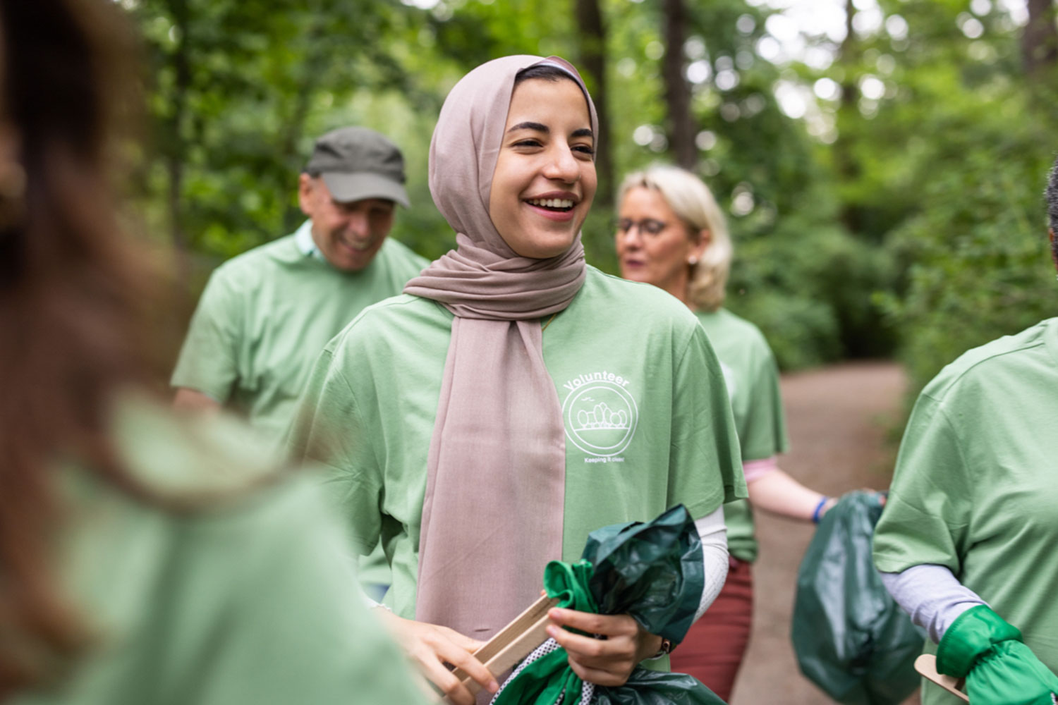 A woman with a headscarf wearing a green T-Shirt and carrying a litter bag