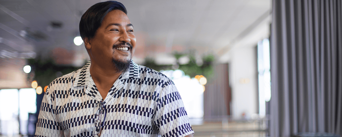 A man is smiling off to the right. He has short brown hair and is wearing a black and white shirt in a pattern that resembles piano keys.