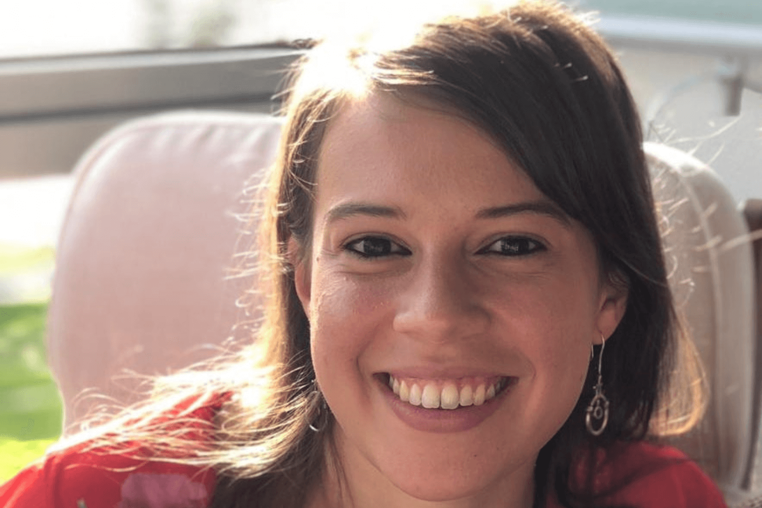 A woman with dark hair slightly longer than shoulder length smiling at the camera, and wearing a red top with floral pattern. 