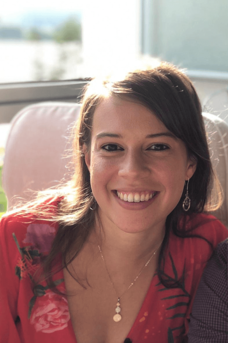 A woman with dark hair slightly longer than shoulder length smiling at the camera, and wearing a red top with floral pattern. 