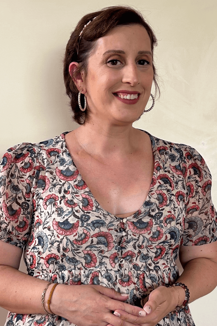 A woman with short brown hair and gold hooped earrings. She is wearing a multicoloured, patterned top. 