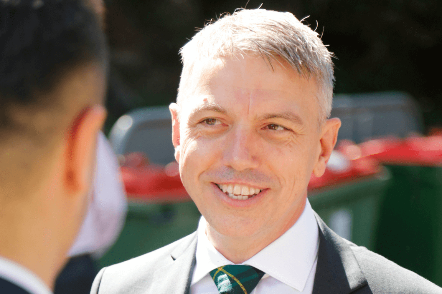 A man in a white short, black jacket and green tie. 