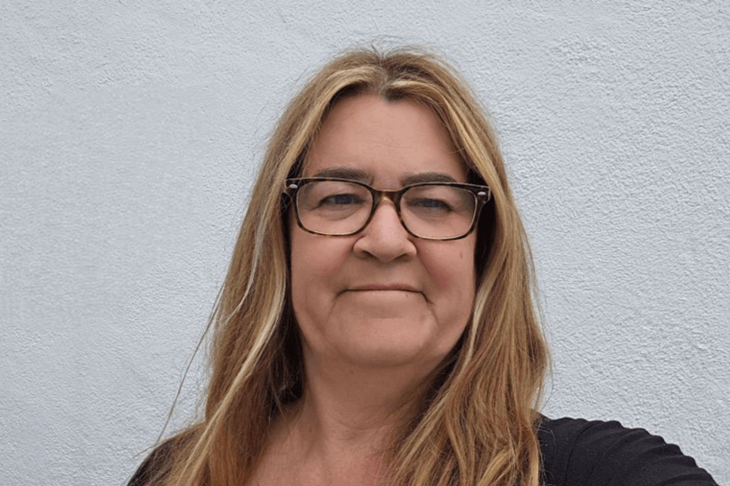 A woman with long hair and glasses. She has on a black top.