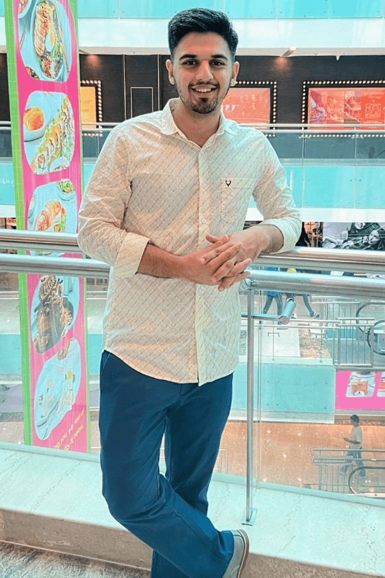 A man with a white shirt and jeans, stood against a balcony railing in a shopping centre. . 