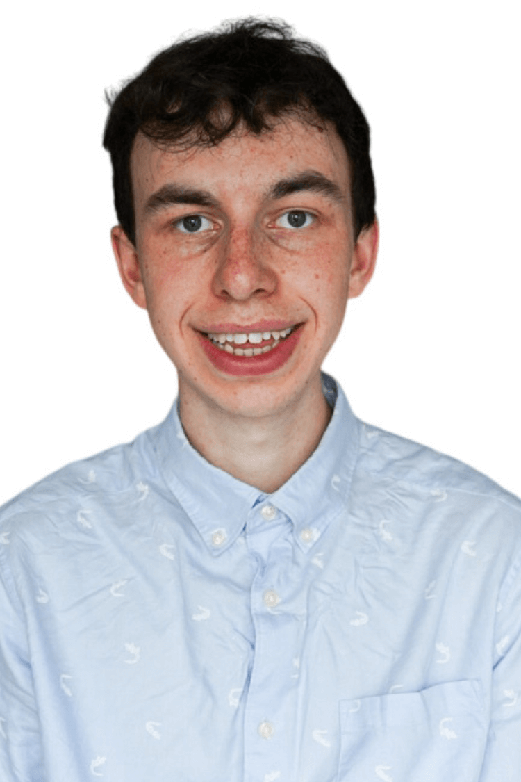 A young man with short curly hair. He is wearing a buttoned up blue shirt. 