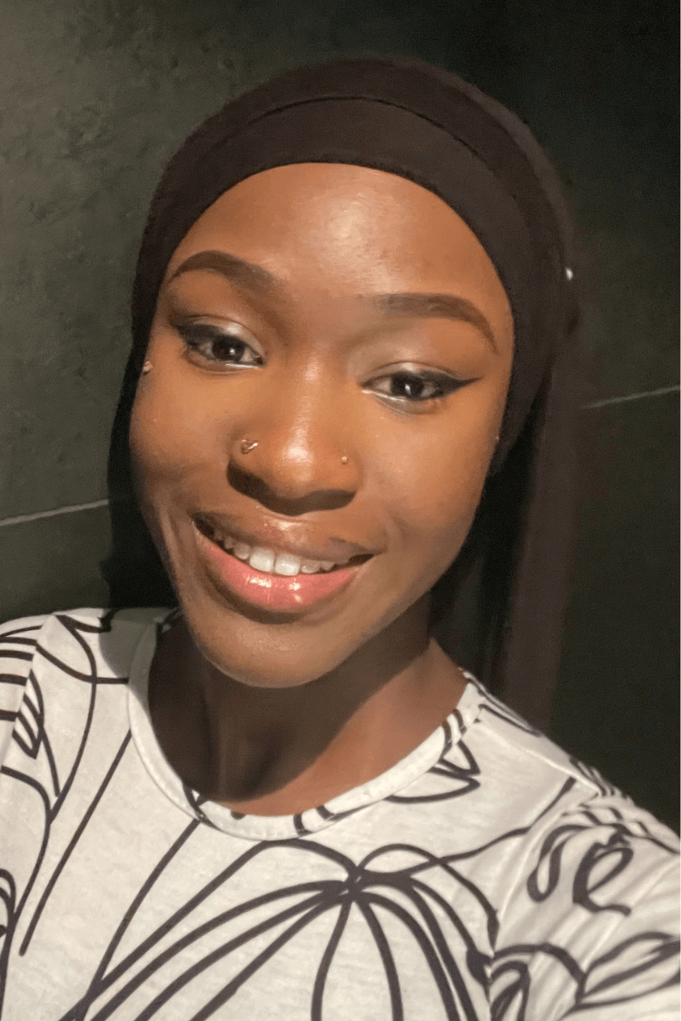 A young girl wearing a black hair band. She is wearing a white blouse with a black linear pattern. 